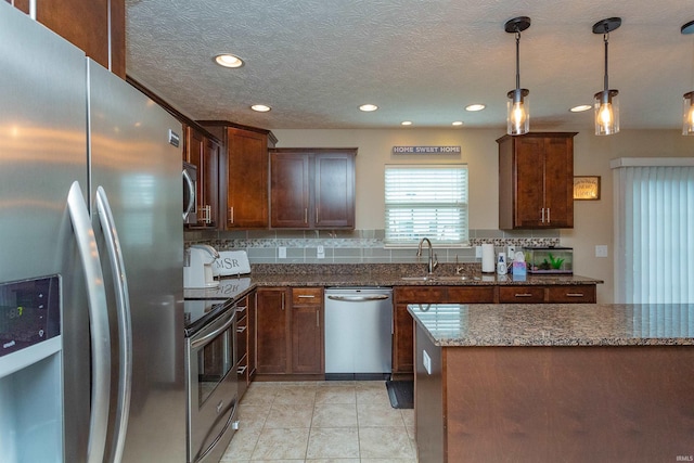 kitchen featuring sink, backsplash, dark stone counters, pendant lighting, and appliances with stainless steel finishes