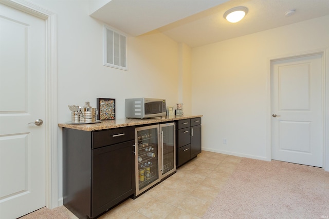 bar featuring dark brown cabinetry, light stone counters, and beverage cooler