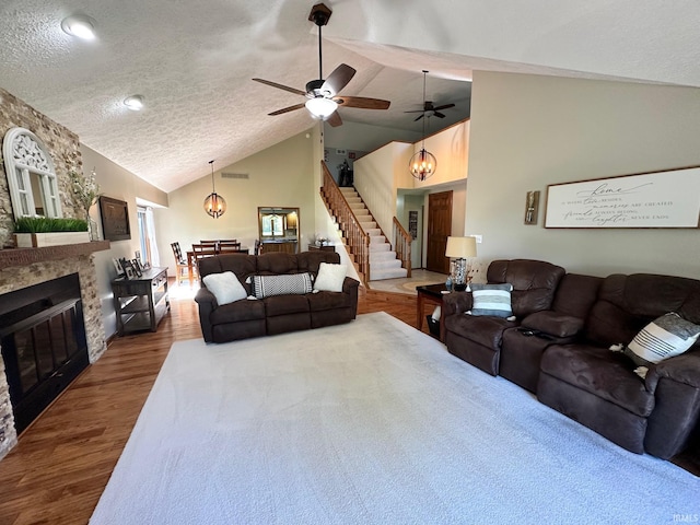 living room with ceiling fan, a stone fireplace, wood-type flooring, lofted ceiling, and a textured ceiling