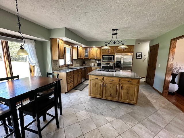 kitchen with sink, backsplash, decorative light fixtures, a kitchen island, and appliances with stainless steel finishes