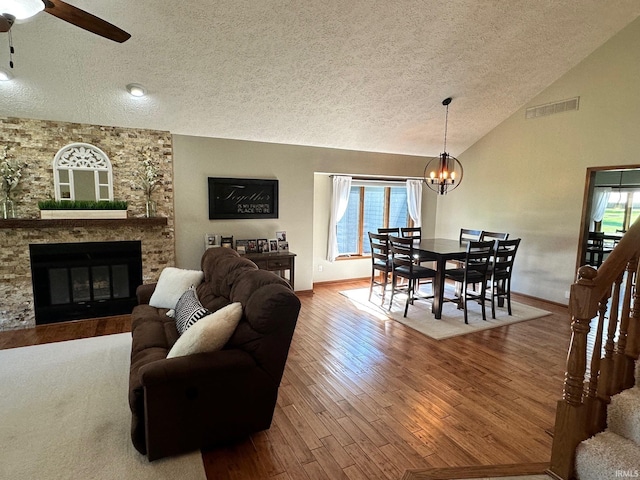 living room with ceiling fan with notable chandelier, hardwood / wood-style flooring, a textured ceiling, a fireplace, and a healthy amount of sunlight