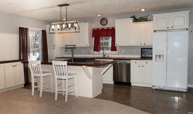 kitchen with a breakfast bar, white cabinetry, stainless steel dishwasher, pendant lighting, and white refrigerator with ice dispenser