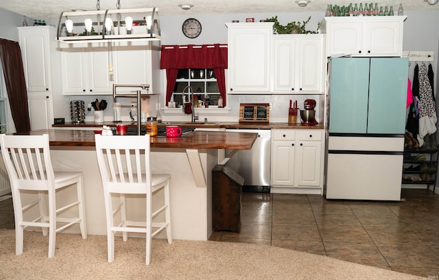 kitchen with butcher block countertops, sink, dishwasher, fridge, and white cabinets