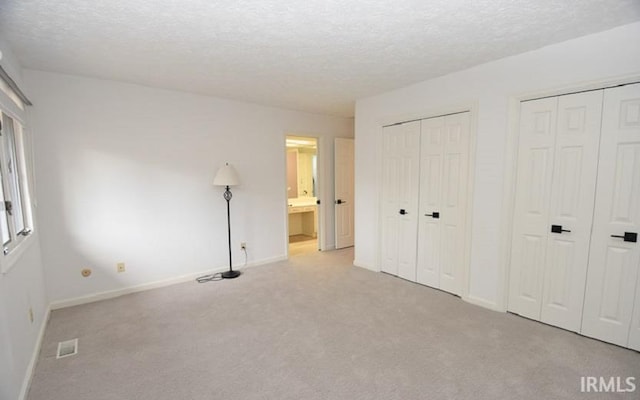 unfurnished bedroom with a textured ceiling, connected bathroom, light colored carpet, and two closets