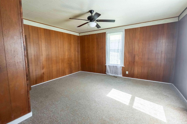 carpeted empty room featuring ceiling fan, wood walls, and crown molding