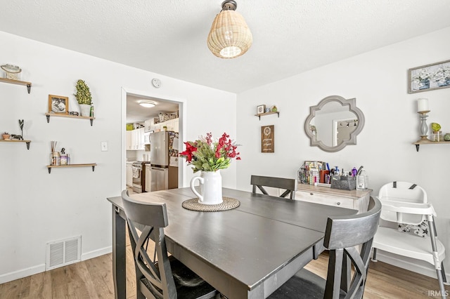 dining space with a textured ceiling and light wood-type flooring