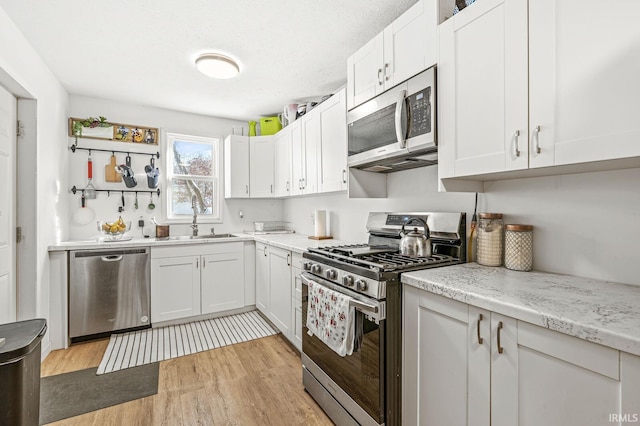 kitchen featuring white cabinets, sink, appliances with stainless steel finishes, light hardwood / wood-style floors, and light stone counters