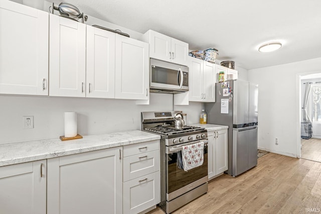 kitchen with light stone countertops, white cabinets, light wood-type flooring, and appliances with stainless steel finishes