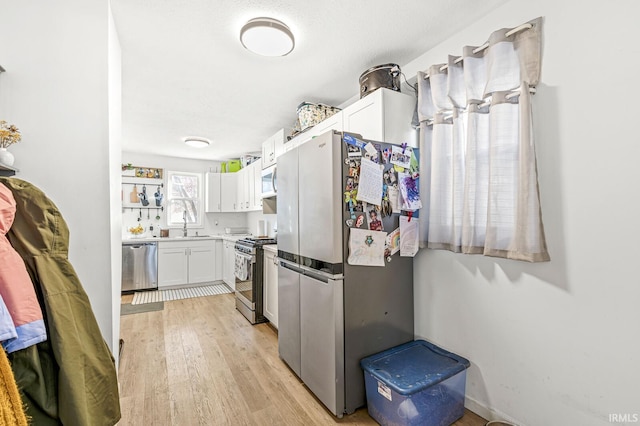 kitchen with white cabinets, appliances with stainless steel finishes, light wood-type flooring, and sink