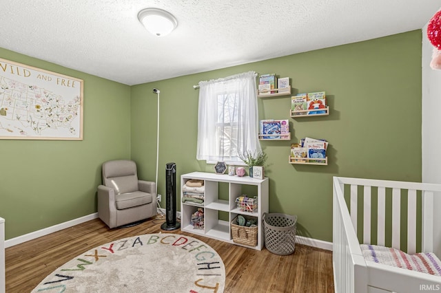 bedroom with a textured ceiling, hardwood / wood-style floors, and a crib