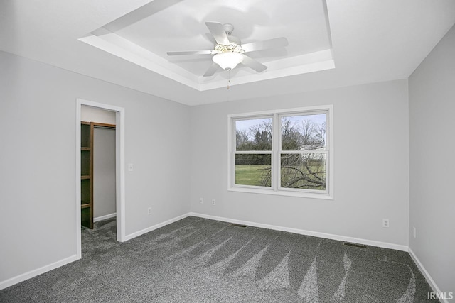 unfurnished bedroom with a closet, a tray ceiling, a spacious closet, and ceiling fan