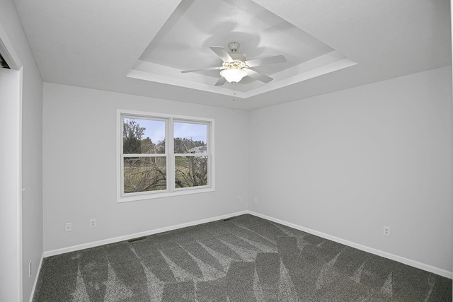 spare room with a raised ceiling, ceiling fan, and dark colored carpet