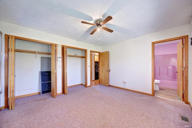 unfurnished bedroom featuring ensuite bath, ceiling fan, light colored carpet, a textured ceiling, and two closets