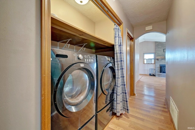 clothes washing area with light wood-type flooring, a textured ceiling, separate washer and dryer, and a brick fireplace