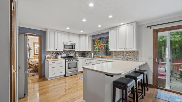 kitchen with sink, tasteful backsplash, white cabinetry, kitchen peninsula, and stainless steel appliances