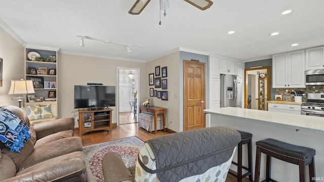 living room with ceiling fan, rail lighting, ornamental molding, and light wood-type flooring