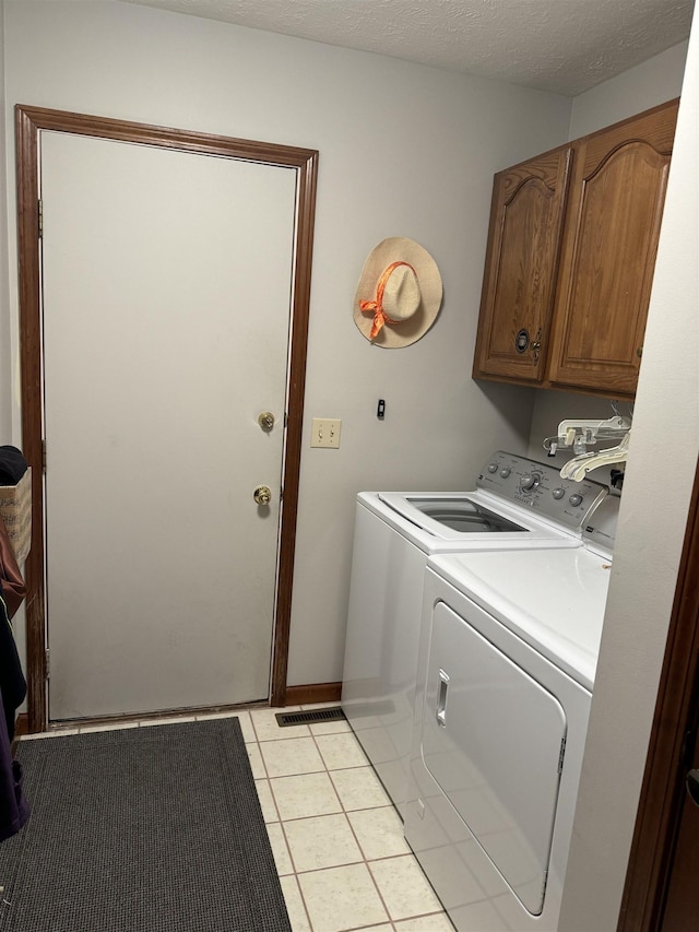 washroom featuring cabinets, light tile patterned floors, a textured ceiling, and washer and clothes dryer