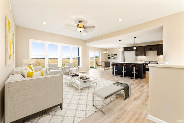 living room with ceiling fan with notable chandelier, light wood-type flooring, and sink