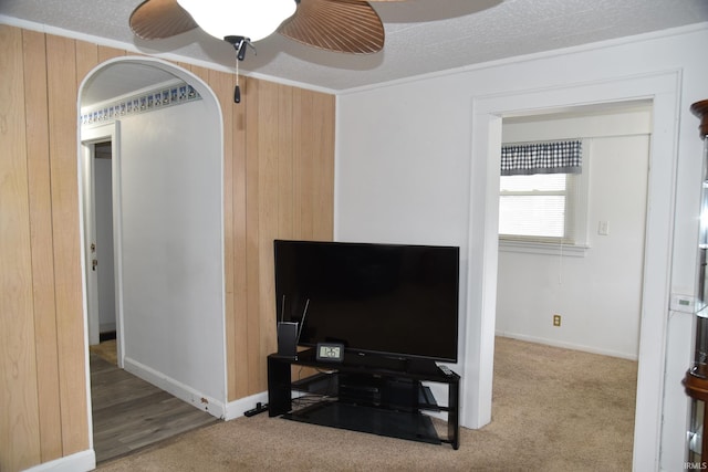 living room with carpet flooring, ceiling fan, crown molding, and wooden walls