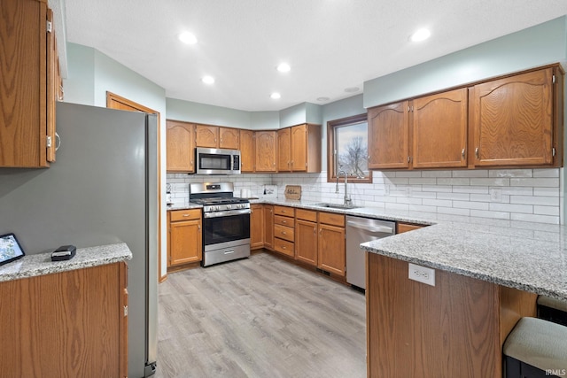 kitchen with sink, light hardwood / wood-style floors, light stone counters, kitchen peninsula, and stainless steel appliances