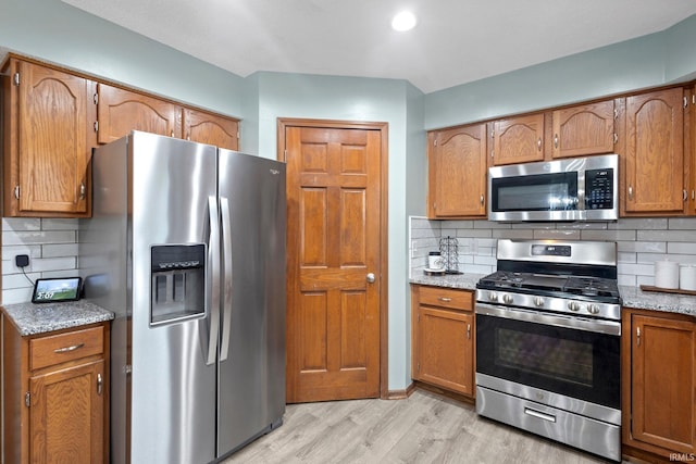 kitchen featuring appliances with stainless steel finishes, backsplash, and light stone counters