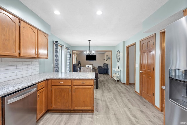 kitchen featuring stainless steel appliances, a notable chandelier, kitchen peninsula, light hardwood / wood-style floors, and decorative backsplash