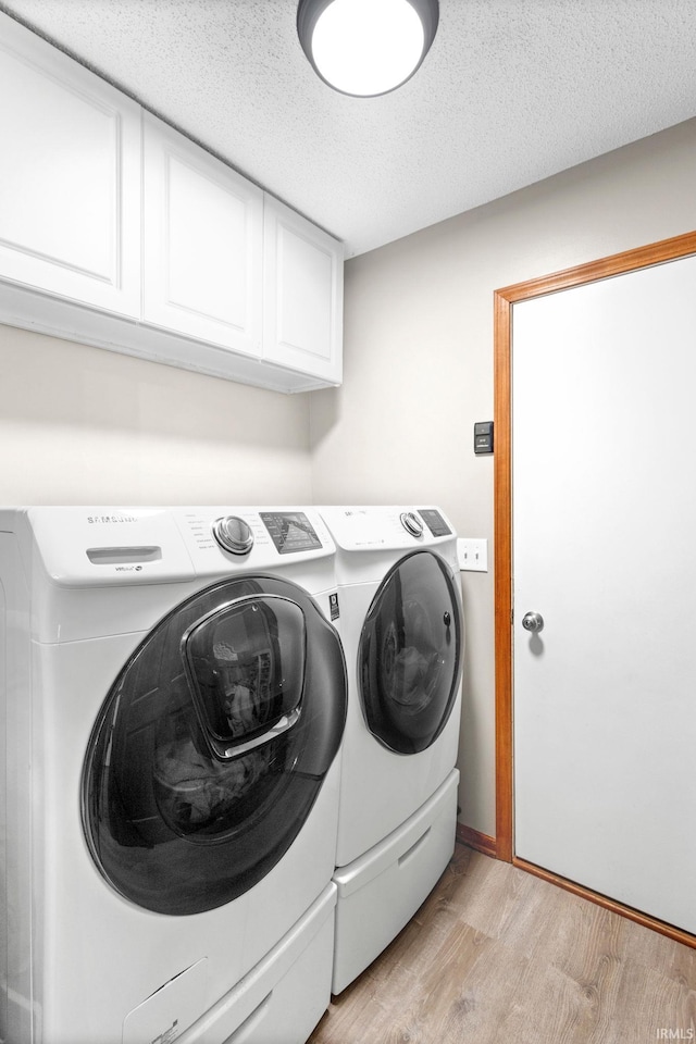 clothes washing area featuring washer and clothes dryer, cabinets, light wood-type flooring, and a textured ceiling