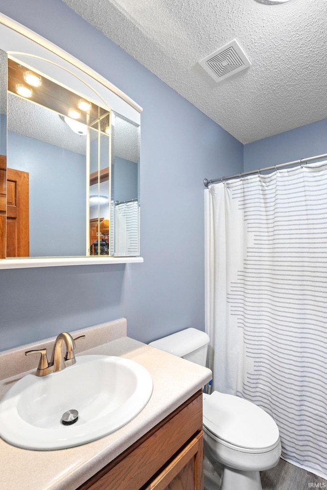 bathroom with vanity, toilet, a textured ceiling, and walk in shower