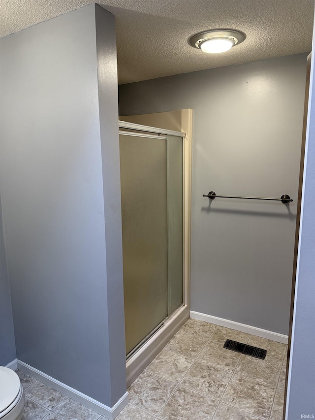 bathroom featuring a textured ceiling, toilet, and a shower with shower door