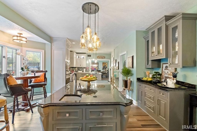 kitchen with light hardwood / wood-style floors, a textured ceiling, a kitchen island with sink, gray cabinets, and hanging light fixtures