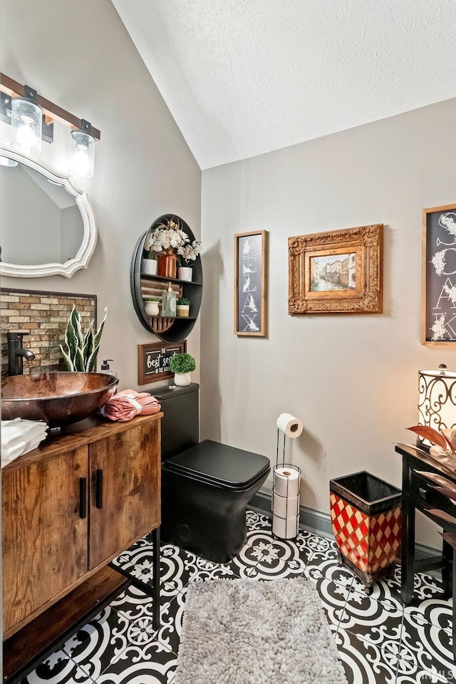 bathroom with vanity, toilet, a textured ceiling, and vaulted ceiling