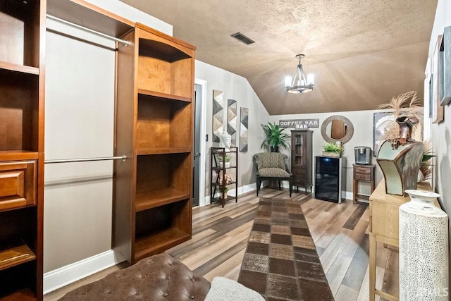 interior space with hardwood / wood-style floors, vaulted ceiling, a textured ceiling, a notable chandelier, and beverage cooler