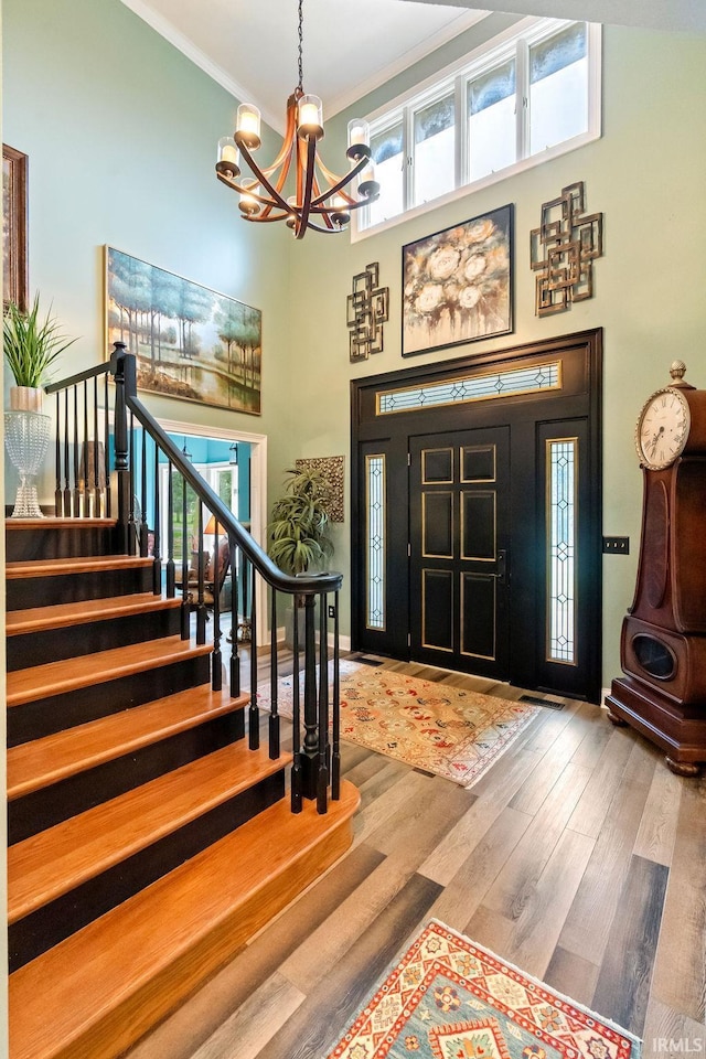 entryway with a high ceiling, hardwood / wood-style flooring, an inviting chandelier, and ornamental molding