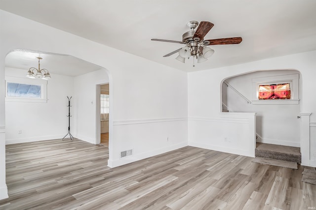 empty room featuring light wood-type flooring, ceiling fan with notable chandelier, and a healthy amount of sunlight