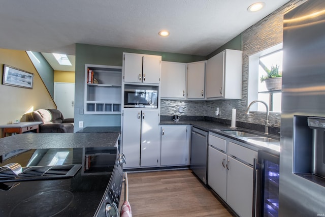 kitchen with sink, wine cooler, a skylight, appliances with stainless steel finishes, and white cabinetry