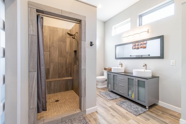 bathroom with hardwood / wood-style floors, toilet, a tile shower, and vanity