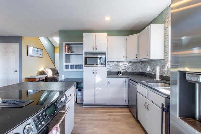 kitchen with white cabinets, sink, decorative backsplash, light wood-type flooring, and appliances with stainless steel finishes