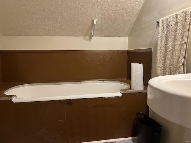 bathroom with a textured ceiling, a tub, sink, and vaulted ceiling