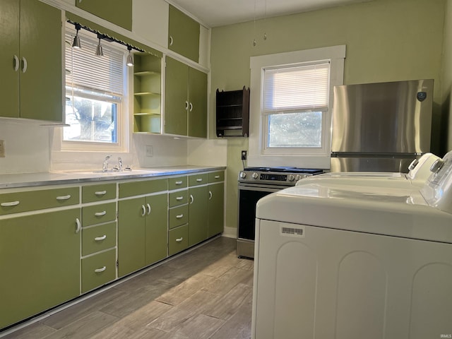 kitchen with green cabinets, sink, stainless steel fridge, range, and washing machine and clothes dryer