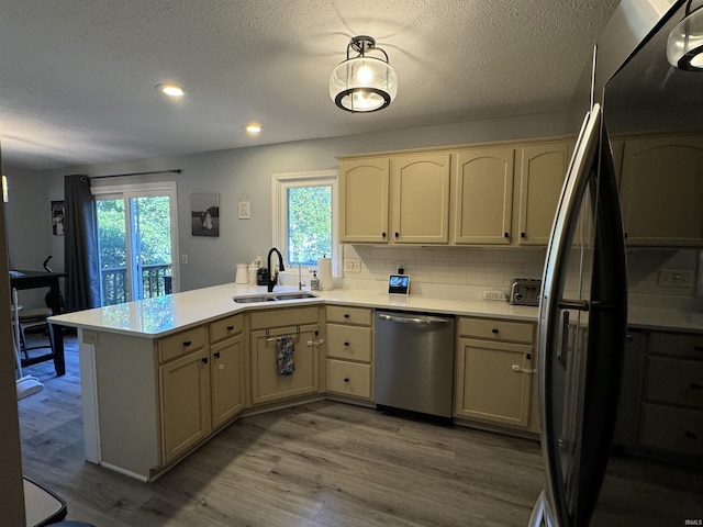 kitchen with kitchen peninsula, tasteful backsplash, stainless steel appliances, sink, and hardwood / wood-style floors