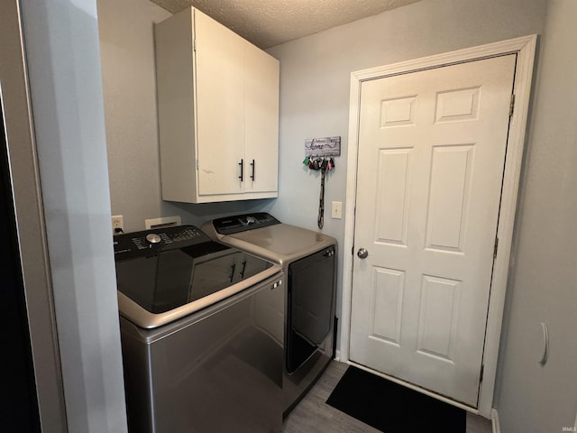 clothes washing area with washer and clothes dryer, cabinets, a textured ceiling, and light hardwood / wood-style flooring