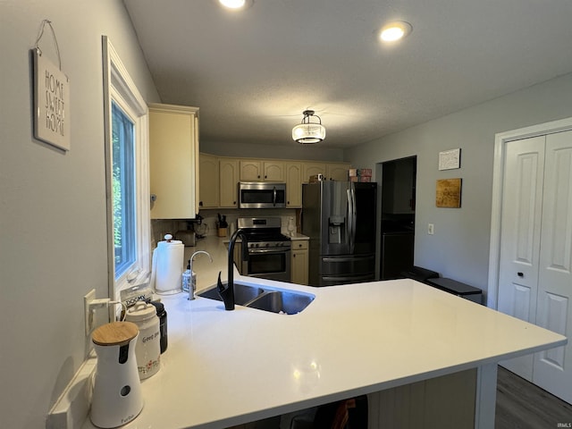 kitchen with cream cabinetry, kitchen peninsula, sink, and appliances with stainless steel finishes