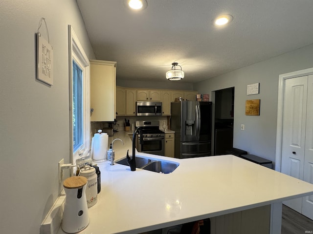 kitchen featuring sink, a textured ceiling, appliances with stainless steel finishes, cream cabinetry, and kitchen peninsula