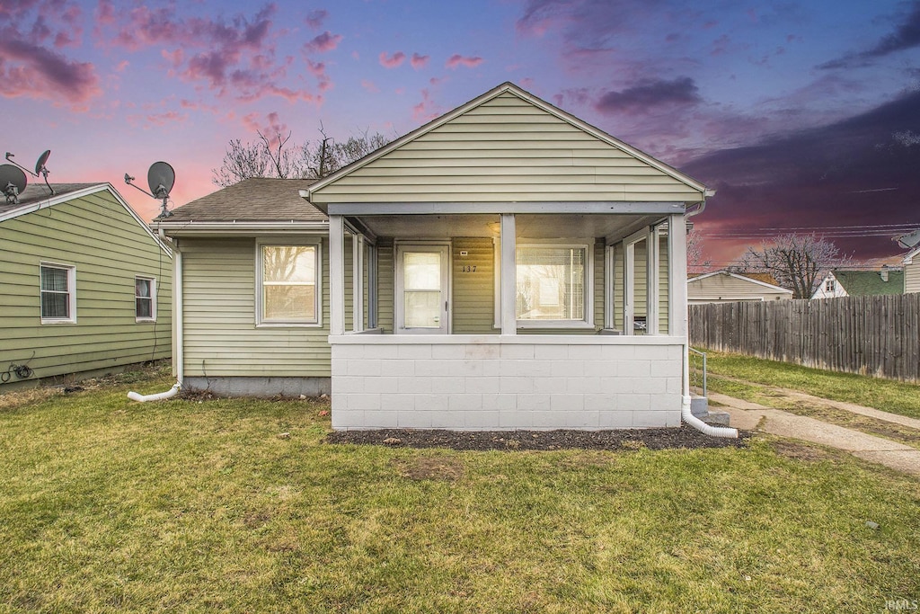 back house at dusk with covered porch and a yard