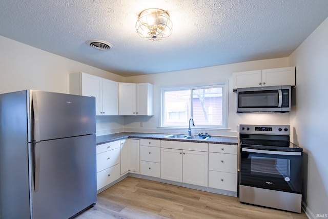 kitchen featuring sink, light hardwood / wood-style flooring, a textured ceiling, appliances with stainless steel finishes, and white cabinetry