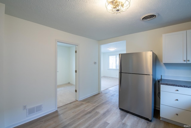 kitchen featuring white cabinets, light hardwood / wood-style floors, a textured ceiling, and stainless steel refrigerator