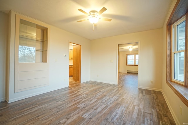 unfurnished room featuring built in shelves, ceiling fan, a baseboard heating unit, and wood-type flooring