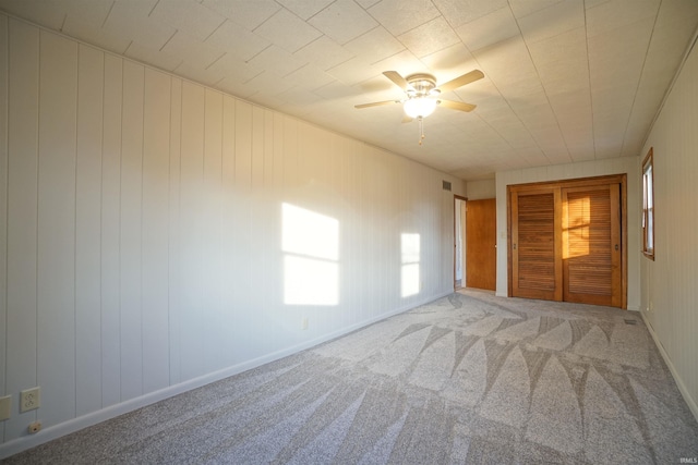 unfurnished bedroom featuring ceiling fan, wood walls, and carpet floors