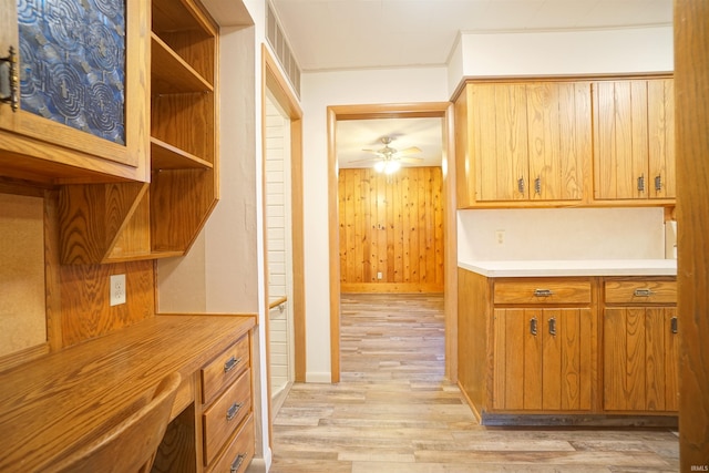 kitchen featuring ceiling fan, light wood-type flooring, and wooden walls