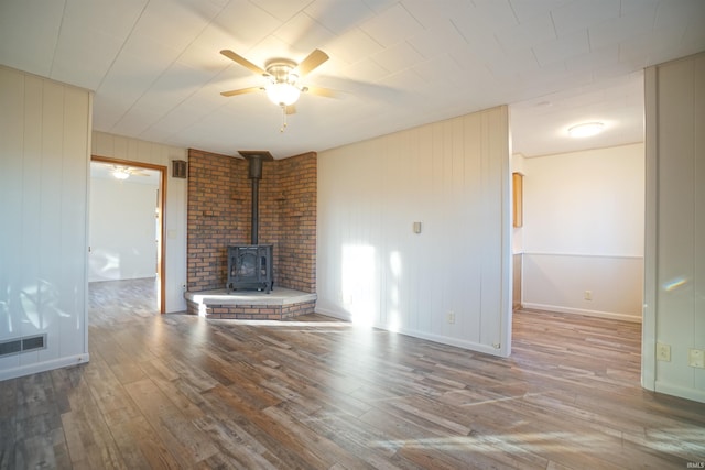 unfurnished living room featuring a wood stove, ceiling fan, hardwood / wood-style floors, and wood walls